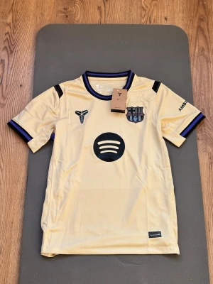FC Barcelona - Away  - Snygg gul FC Barcelona matchtröja med svarta och blå detaljer. Tröjan har klubbmärke, Nike-logga och Spotify som sponsor framtill samt UNHCR-tryck på ryggen. Tillverkad i lätt och ventilerande material, perfekt för fotboll eller träning.