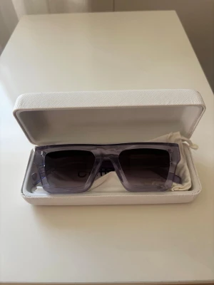 Lila solglasögon CHIMI x H&M - Säljer ett par trendiga solglasögon från CHIMI x H&M med rektangulära bågar i transparent lila plast. Kommer i originalvitt fodral med logga och tillhörande tygpåse. Perfekta för att lyfta din look med en cool touch.