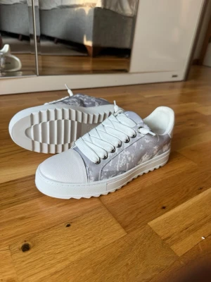 Vita och grå sneakers från Numeris - Snygga sneakers från Numeris i vitt och grått med coolt mönster på sidorna. Skorna har vita snören, grov sula och ovandel i textil och syntet. Perfekta för dig som vill ha en stilren men ändå unik look. Obs stora i storlek 
