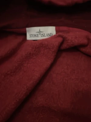 Vinröd hoodie från Stone Island - Snygg vinröd hoodie från Stone Island med klassisk logotyp på bröstet och justerbar huva med dragsko. Tillverkad i mjukt material som känns skönt mot huden. Perfekt för dig som gillar streetwear och vill sticka ut med en ikonisk look.