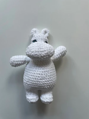 Virkad vit Mumin-figur - Säljer en handgjord, virkad Mumin-figur i mjukt vitt garn. Figuren har stora blå ögon, rund mage och utstickande nos samt små öron. Perfekt som dekoration eller mysig maskot. Passar dig som gillar Mumin och unika handgjorda saker. 23 cm