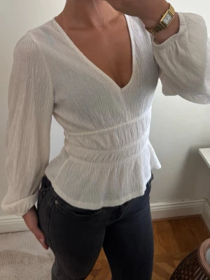 Vit omlottblus med v-ringning - Säljer en stilren vit omlottblus som är slutsåld och super elegant. Den har två super små hål lite längre ner som knappt syns.