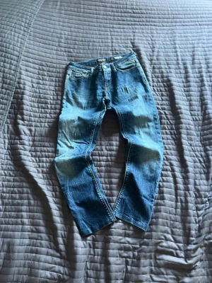  Replay jeans - Säljer ett par blå jeans med raka ben och slitna detaljer. Jeansen har klassisk femficksdesign, knappgylf och är tillverkade i denim. Perfekta för en avslappnad och trendig look.