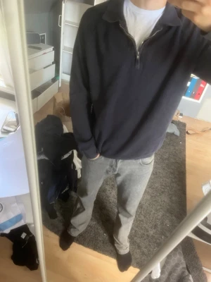 Mörkblå ziptröja med krage - Säljer en mörkblå långärmad ziptröja med krage. Tröjan har ribbade muddar vid ärmslut och nederkant samt en halv dragkedja framtill. Perfekt för lager på lager och enkel att matcha med jeans eller byxor.