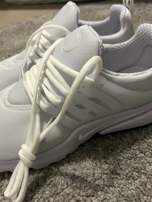 Nike vita Presto sneakers - Fräscha vita Nike Presto sneakers med mesh-ovandel och plastdetaljer på sidorna. Skorna har en låg siluett, klassiska snörningar och diskret Swoosh-logga på sidan. Perfekta för en clean och sportig look.