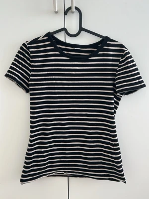 Svartvit randig t-shirt - En klassisk svartvit randig t-shirt med rund hals och korta ärmar. T-shirten har smala horisontella ränder och är i mjukt, bekvämt material som passar perfekt till jeans eller kjol.