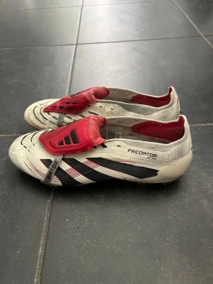 Adidas Predator Elit - Säljer ett par Adidas Predator Elite FT FG i storlek 42 2/3. Det här är Elite-modellen, alltså toppversionen i Predator-serien. Skorna är i mycket bra skick och har endast använts ett fåtal gånger. Dobbarna har minimalt slitage och både originalinnersulor samt extra skosnören medföljer. Det finns mindre kosmetiska märken från spel på konstgräs, vilket syns på bilderna, men det påverkar varken prestanda eller funktion. Säljs utan originalkartong. Hör gärna av dig om du har några frågor eller vill
