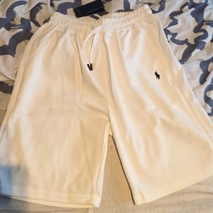 Vita shorts från Polo Ralph Lauren - Snygga vita shorts från Polo Ralph Lauren med klassisk logga broderad på benet. Shortsen har dragsko i midjan för skön passform och är tillverkade i mjuk bomull. Perfekta för sommardagar och chill häng.
