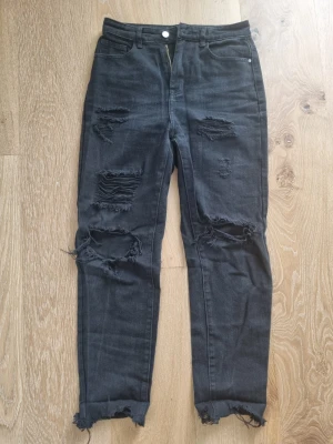 Svarta slitna jeans - Säljer ett par svarta high rise mom jeans med slitningar och hål på framsidan samt fransiga benslut. Innermått: 64 cm midja: ca 70 cm
