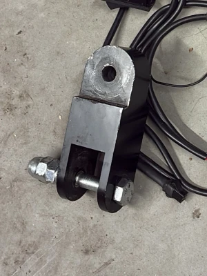 Höjningssats - Säljer ett robust svart metallfäste med bult och muttrar, troligen för maskin eller fordon. Fästet har en genomgående axel och flera anslutande kablar. Perfekt för dig som behöver reservdel eller vill bygga om något tekniskt.