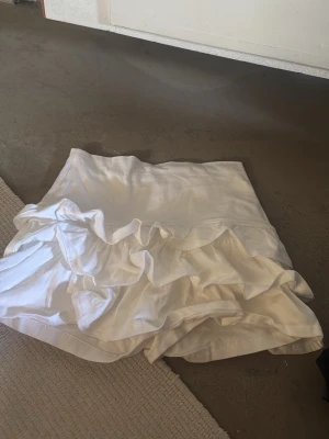 Vit volangljol subdued - Supersöt vit skort med volangdetaljer framtill och shorts under kjolen. Perfekt för en trendig och bekväm look. Tillverkad i ett mjukt och lätt tyg som ger en luftig känsla. Passar perfekt till sommarens outfits.
