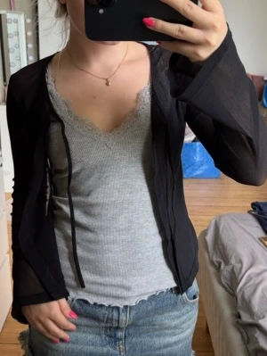 Svart mesh bolerotopp med knyt - Trendig svart bolerotopp i mesh med långa ärmar och knyt framtill. Perfekt att styla över ett linne eller topp för en cool lager-på-lager-look. Tunn och luftig, ger en snygg siluett och passar till både jeans och kjol🙌🏼🤩Vet tyvärr dock ej vart den är ifrån då det inte finns en lapp i den!!