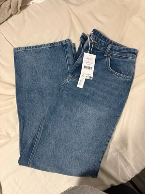 Raka blå jeans med medelhög midja - Säljer ett par klassiska raka jeans från H&M i blå denim med medelhög midja. Jeansen har fem fickor och stängs med dragkedja och knapp. Perfekta till vardagslooken och passar till det mesta. Materialet är 100% bomull för en skön och avslappnad känsla.
