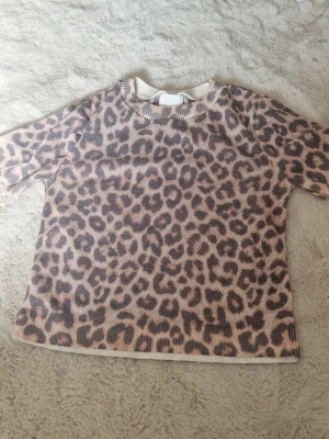 Leopardmönstrad topp, H&M - Säljer en kortärmad topp från H&M med leopardmönster i beige och bruna toner. Toppen har rund halsringning och ribbade kanter vid ärmslut och nederkant. Perfekt för dig som gillar djurmönstrat och vill sticka ut lite extra. Tröjan är tunn och funkar på sommaren.