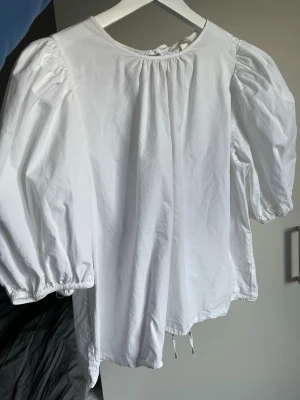 Vit blus med puffärm och knytning - Säljer en vit blus med puffiga trekvartsärmar och rund hals. Blusen har tre dekorativa knytband i ryggen. Luftigt och skönt material. Perfekt till våren/sommaren