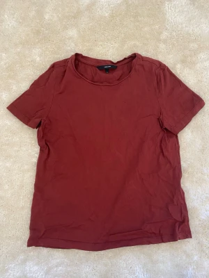 Mörkröd basic t-shirt från Vero Moda - En enkel mörkröd t-shirt från Vero Moda med rund halsringning och korta ärmar. Tillverkad i mjuk bomull för en skön känsla. Perfekt till jeans eller shorts för en avslappnad look. Finns två små hål men det är inget som syns när man har på sig den