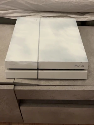 Vit PlayStation 4 konsol - Säljer en stilren vit PlayStation 4 från Sony. Konsolen har en snygg, kantig design och är tillverkad i plast. Perfekt för gaming och streaming, passar dig som vill ha en clean setup hemma.
