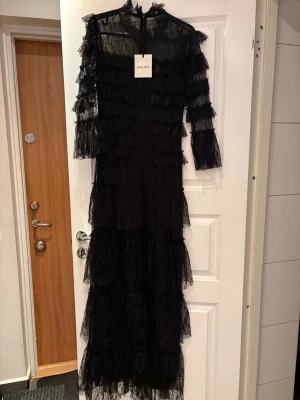 Svart lång spetsklänning från Bymalina - Svart långklänning från Bymalina i spets med volangdetaljer och trekvartsärm. Klänningen är använd en gång och är som ny. Nypris på denna klänning är ca 4500.