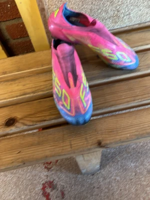 Adidas X Speedflow rosa fotbollsskor - Säljer ett par Adidas X Speedflow fotbollsskor i en riktigt snygg rosa färg med blå och gula detaljer. Skorna har en strömlinjeformad design utan snörning och är tillverkade i syntetmaterial för bästa känsla och lätthet på planen.