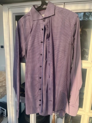 Lila rutig skjorta från Eton - Snygg lila strykfri rutig skjorta från Eton i slim fit. Skjortan har klassisk krage, långa ärmar och svarta knappar framtill. Tillverkad i mjuk bomull som känns skön mot huden. Perfekt för dig som vill ha en stilren och modern look. Storlek 16(41) slim. 