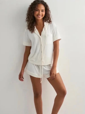 Vit kortärmad pyjamas med shorts - Den har lite missfärgningar, samma som på den rosa toppen jag har uppe! Säljer en fräsch vit pyjamas med kortärmad skjorta och matchande shorts. Skjortan har knappar framtill och en bröstficka, medan shortsen har dragsko i midjan för skön passform. Använda få antal ggr