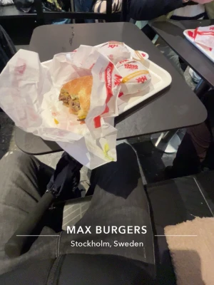 Hamburgermål från Max Burgers - Säljer ett hamburgermål från Max Burgers med en klassisk hamburgare i ljust bröd, inslagen i vitt papper med röd logga. Tillbehör och dryck kan ingå. Perfekt för dig som gillar snabbmat och vill ha något gott och mättande.
