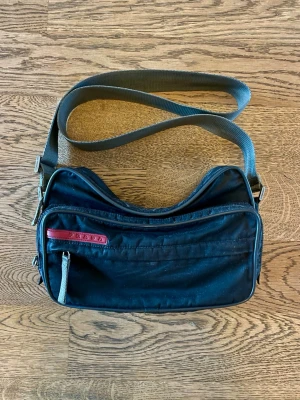 Vintage Prada Sport Väska - Svart Vintage Prada Sport väska. Sparsamt använd, i jättefint skick. Köpt på Ettresex i Stockholm, kvitto finns. Säljs pga minskad användning. Bara att höra av dig vid intresse, frågor eller önskan om fler bilder! Mvh