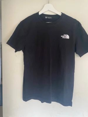 Svart The North Face t-shirt - Säljer en svart t-shirt från The North Face med liten logga på bröstet och stor grafisk print med berg och koordinater på ryggen. Klassisk passform och rund halsringning. Perfekt för dig som gillar outdoor-vibbar och streetstyle. Köpt i Bulgarien 