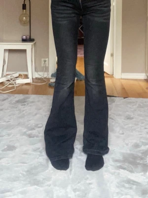 Svarta bootcut jeans med fickdetaljer - Säljer ett par svarta bootcut jeans med snygga fickdetaljer bak och utsvängda ben. Jeansen har klassisk femficksmodell och är tillverkade i ett stretchigt denimtyg som sitter bekvämt. Perfekta för dig som gillar en retroinspirerad look.