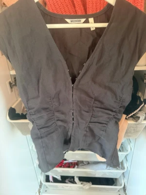 Svart v-ringad väst från Weekday - Snygg svart väst från Weekday med v-ringning och figurnära passform. Västen har knappar framtill och är tillverkad i ett lätt bomullsmaterial. Perfekt att styla över en t-shirt eller skjorta för en trendig look. i stolek S!! 