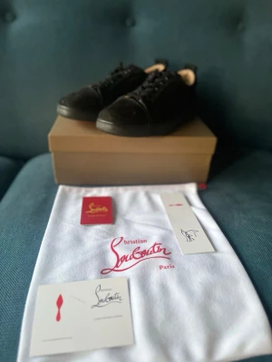 Svarta sneakers från Christian Louboutin - Snygga svarta sneakers från Christian Louboutin med klassisk röd sula och diskret logga. Skorna har lågt skaft, svarta skosnören och är tillverkade i en mix av läder och textil. Sulan kan behövas tvätta men annars är de i riktigt fint skick