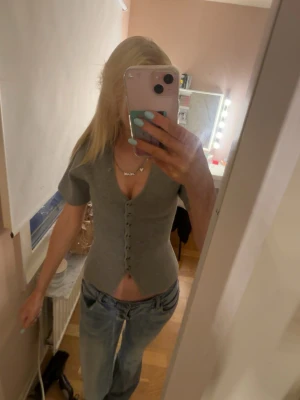 Grå ribbad topp med knappar - Snygg grå ribbad topp med v-ringning och korta ärmar. Toppen har en figurnära passform och knappar hela vägen framtill. 