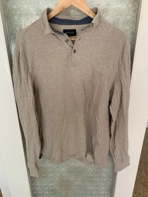 Beige långärmad henley från Howick - Snygg beige långärmad henley från Howick med klassisk krage och knappar vid halsen. Tillverkad i mjuk bomull som känns skön mot huden. Perfekt för dig som gillar en enkel men stilren look.