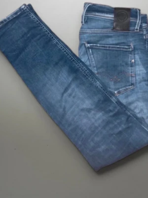 Blå slim fit jeans från Replay - Snygga blå slim fit jeans från Replay med klassisk femficksdesign och läderpatch bak i midjan. Jeansen har en tvättad look med subtila slitningar och är tillverkade i mjukt denimtyg för en bekväm känsla.