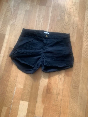 Svarta shorts med fickor, H&M strl 42 - Svarta shorts i klassisk modell med två framfickor och två bakfickor. Stängs med knapp och dragkedja framtill. Perfekta för varma dagar och har en enkel, stilren look. Materialet känns som bomull och passformen är normal.