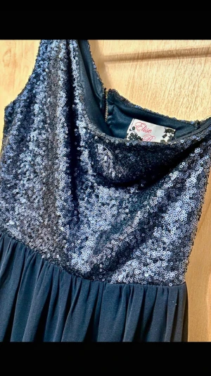 BALKLÄNNING 2026 – GLITTRIG ONE SHOULDER  - Mörkblå långklänning från Elise Ryan med paljettöverdel som glittrar sjukt fint ✨ Perfekt till bal, gala eller fest! • One shoulder • Flowy kjol • Dragkedja  Stl EU 38 (S/M) Längd - ca 139cm Byst - ca 36cm Axelband - ca 5cm