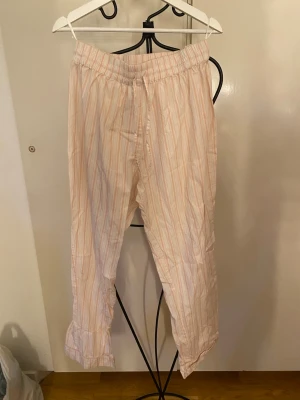Randiga pyjamasbyxor från Åhléns - Säljer ett par mjuka pyjamasbyxor från Åhléns i storlek M. Byxorna har vita och ljusrosa ränder, elastisk midja och är tillverkade i ett lätt och bekvämt material. Perfekta för mysiga hemmakvällar.
