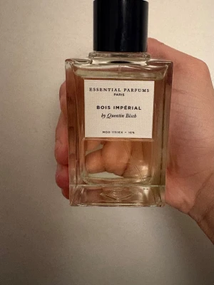 Bois Impérial parfym Essential Parfums - Bois Impérial från Essential Parfums är en elegant parfym i en stilren, genomskinlig glasflaska med svart lock. Doften är skapad av Quentin Bisch och flaskan har en modern, minimalistisk design med tydlig etikett framtill. Mängd: 95/100 ml. 