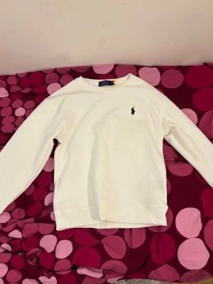 Vit sweatshirt från Polo Ralph Lauren - Aldrig använd. Funkar för både tjejer oxh killar. Säljer en stilren vit sweatshirt från Polo Ralph Lauren med klassisk broderad logga på bröstet. Tröjan har rund halsringning, långa ärmar och ribbade muddar. Perfekt för en clean och avslappnad look.