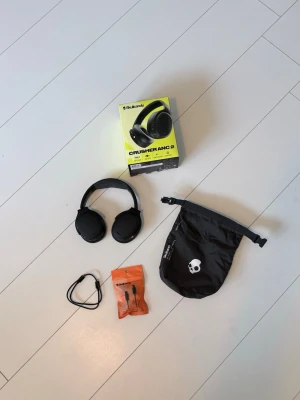 Skullcandy Crusher ANC 2 hörlurar - Säljer ett par svarta Skullcandy Crusher ANC 2 over-ear hörlurar med aktiv brusreducering. Hörlurarna har mjuka öronkuddar, justerbar båge med tygdetalj och flera knappar för kontroll. Medföljer originalförpackning, kabel och svart förvaringspåse. Ny pris 2300kr