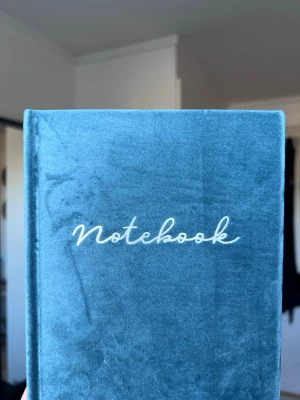 Blå sammetsanteckningsbok - Anteckningsbok med mjukt blått sammetsomslag och texten 'Notebook' broderad i vitt på framsidan.