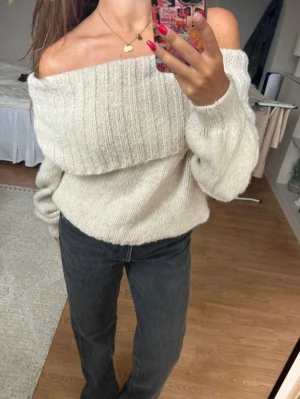Off shoulder stickad tröja i beige - Superfin stickad tröja i beige med off shoulder-modell och bred ribbad kant upptill. Tröjan har en lös och mysig passform med långa ärmar och är perfekt för lager-på-lager. Passar till både jeans och kjol. Använd 1 gång