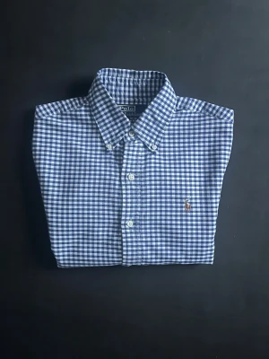 Blårutig skjorta från Polo Ralph Lauren - Klassisk blårutig skjorta från Polo Ralph Lauren i slim fit-modell. Skjortan har button-down krage, vita knappar och broderad logga på bröstet. Perfekt nu inför sommaren. Tveka inte med frågor eller prisförslag 