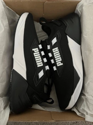 Puma Skor - • Skick: Helt nya, aldrig använda – i originalkartong • Modell: Puma Retaliate 3 • Storlek: EU 39 (UK 6 / US 7 / 25 cm) • Färg: Svart/Vit – stilren och lätt att matcha • Komfort: SoftFoam+ sula för extra dämpning hela dagen • Användningsområde: Perfekta för vardag, promenader, jobb, gym, resor eller lätt träning • Passform: Unisex – passar både män och kvinnor • Design: Sportig och modern look som passar alla outfits