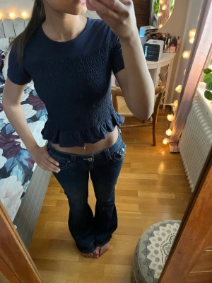 Mörkblå croppad topp med volang - Säljer en mörkblå croppad topp med korta ärmar och volangkant nedtill. 