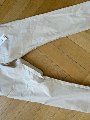 Beige chinos, Oanvända Etiket kvar  - Snygga beige chinos med normal passform och klassisk design. Perfekta för en clean och stilren look. Tillverkade i mjukt bomullsmaterial som känns skönt mot huden. Enkla att matcha med både t-shirt och skjorta. Etikett sitter kvar oanvända. NYPRIS 899kr