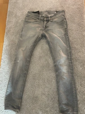 Dondup George - Tja! Säljer ett par gråa Dondups med slitningar och tvättade detaljer i modellen George. Jeansen har fem fickor och en smal passform. Perfekta för dig som gillar en avslappnad och trendig stil. Ända defekten är ett litet hål i skrevet men går lätt att fixa!