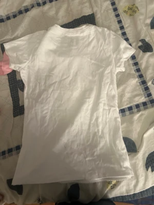 Vit t-shirt med döskalle och dragkedja - Cool vit t-shirt med glittrig döskalle framtill och dekorativ dragkedja längs ena sidan. T-shirten har korta ärmar och rund halsringning. Perfekt för dig som gillar edgy detaljer och vill sticka ut.
