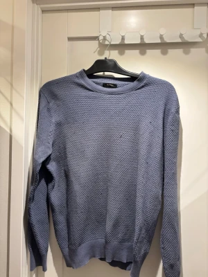Blå stickad tröja Massimo Dutti | M - Snygg blå stickad tröja från Massimo Dutti i bomull och ull. Tröjan har rund halsringning, diskret strukturmönster och ribbade muddar vid ärmslut och nederkant. Perfekt för lager-på-lager och enkel att matcha med jeans eller chinos.