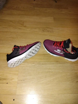 Röda Skechers sneakers med svarta detaljer fint skick 37/38 - Snygga sneakers från Skechers i rött med svarta detaljer och vita sulor. Skorna har röda snören och en stor silverfärgad Skechers-logga på sidan. Ovandelen är i meshmaterial för bra andningsförmåga och komfort. Fint skick 37/38
